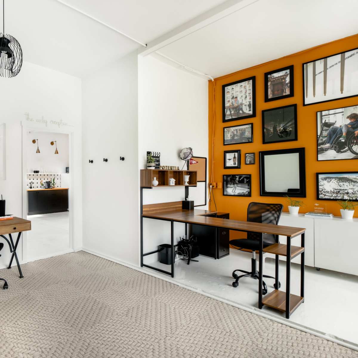 A modern office space featuring two workstations, a large wall with framed photographs, and a combination of light and dark décor elements.