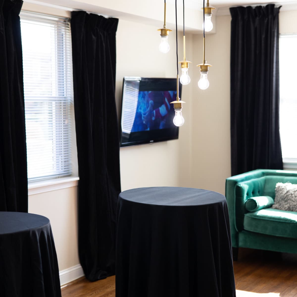 A well-lit room featuring two tall black tables, a green sofa, and a television mounted on the wall.