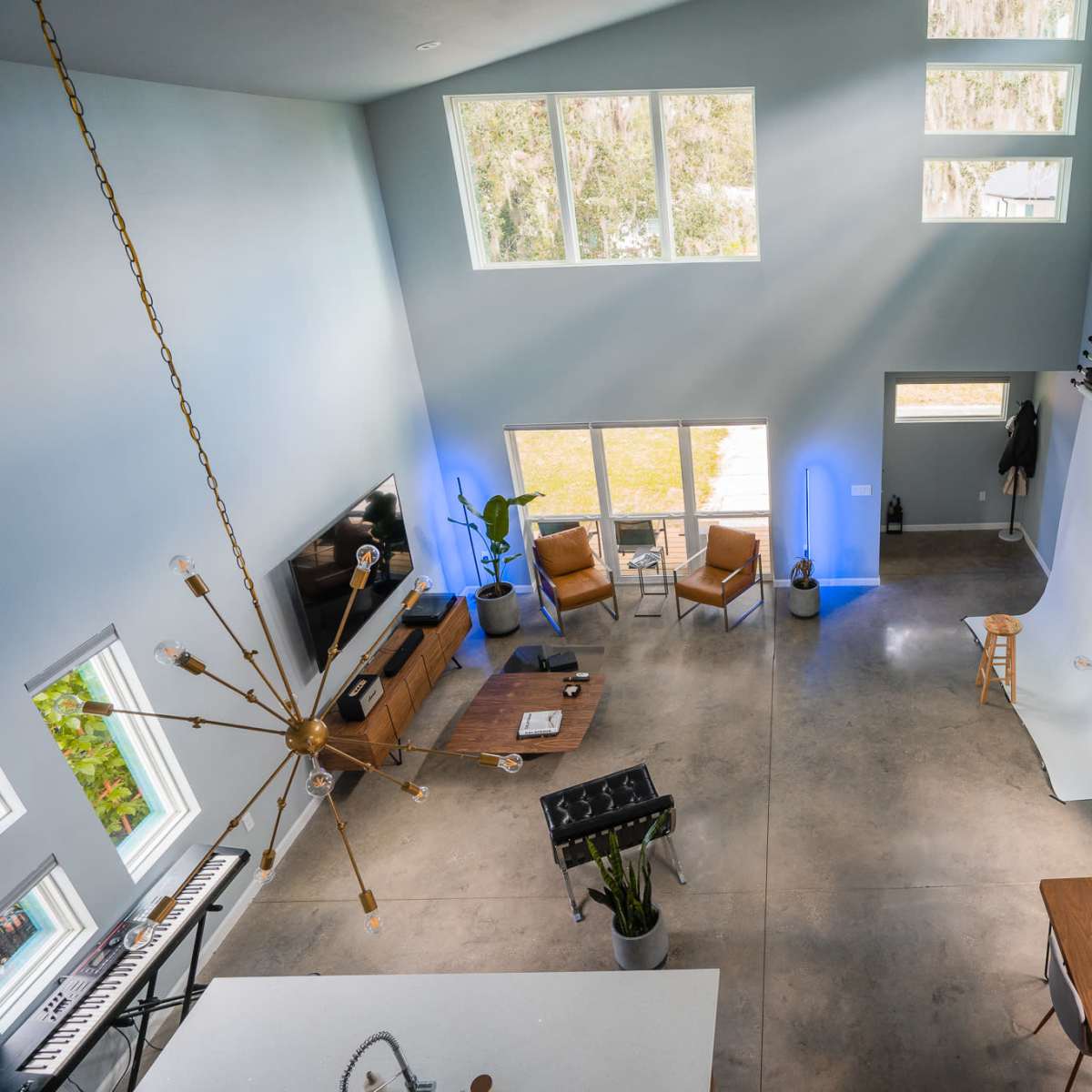A spacious room with high ceilings, large windows, and a mix of modern furniture, including chairs, a dining table, and studio equipment.