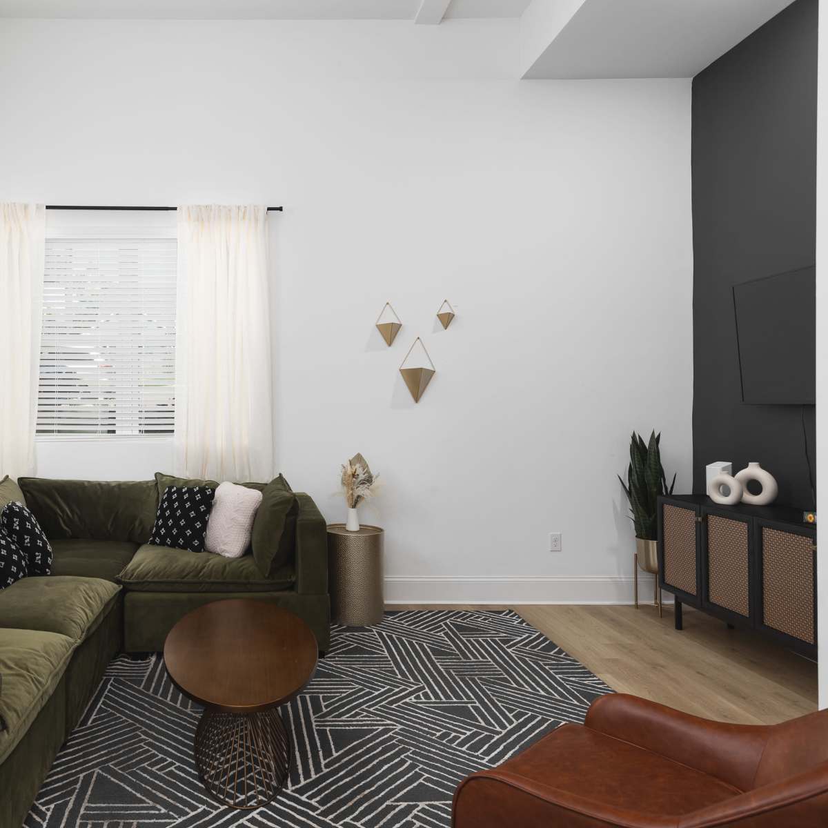 A modern living room featuring a green sectional sofa, a round wooden coffee table, framed artwork on the wall, and geometric decor.