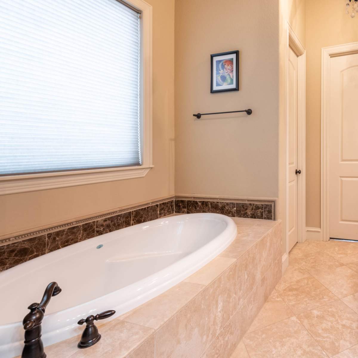A bathroom featuring a white bathtub, a beige countertop with dark faucet fixtures, and a door leading to another room.