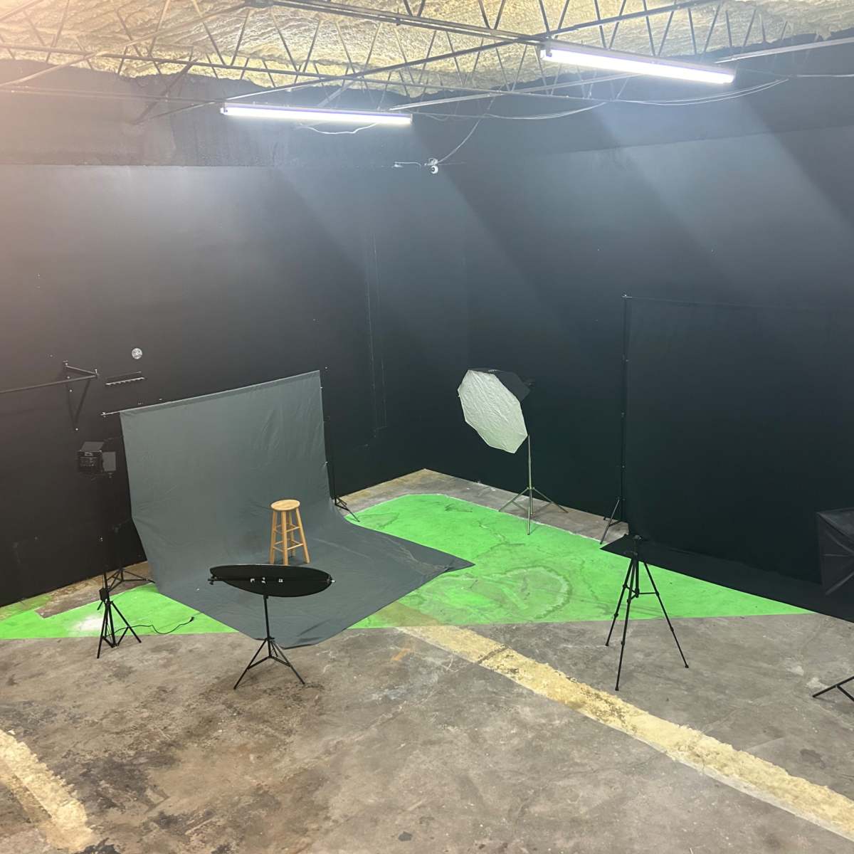 A photography studio with various equipment, including backdrops, lighting setups, and a stool placed on a green floor.