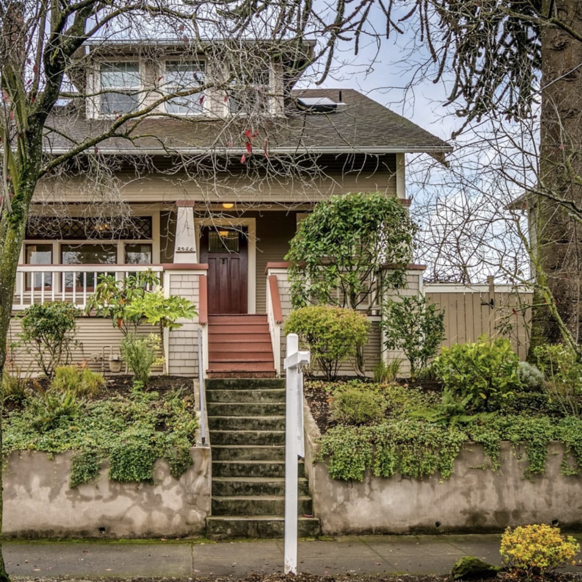 A two-story house with a front porch and landscaped garden is shown, featuring stairs leading up to the entrance.