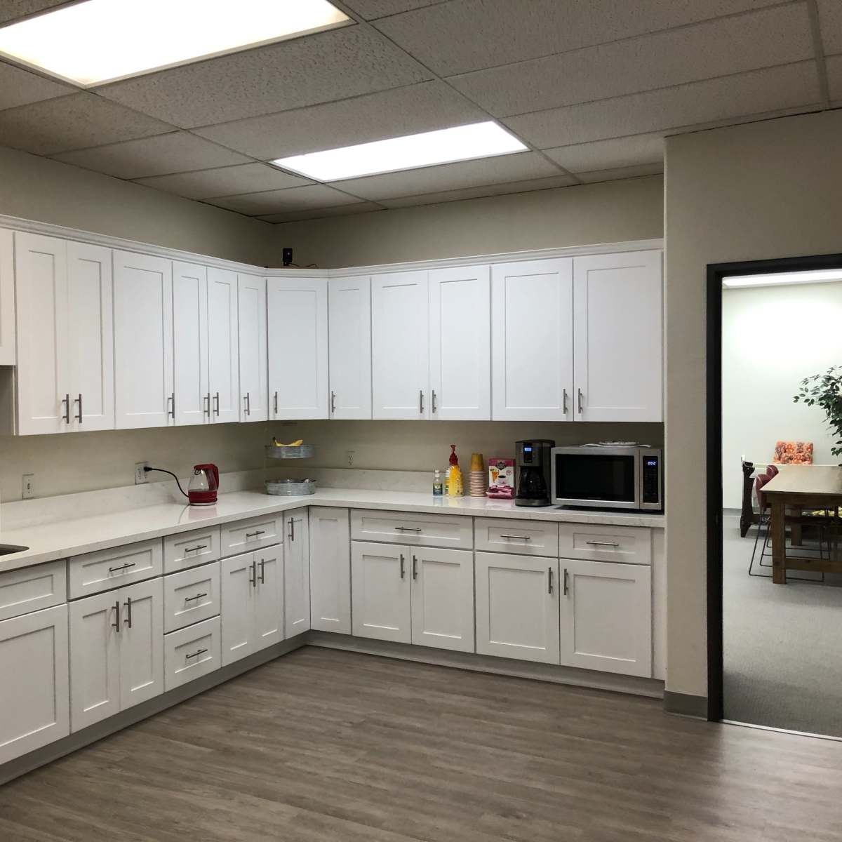A modern kitchen with white cabinetry, a sink, a countertop, and appliances including a microwave and a coffee maker.