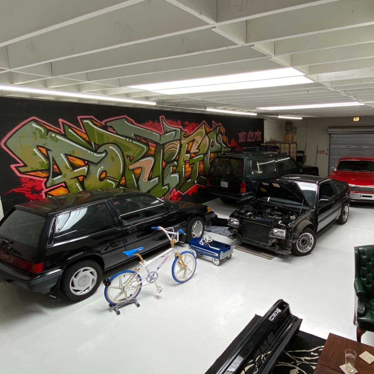 The garage features several parked cars, a motorcycle, bicycles, and a large wall adorned with colorful graffiti.