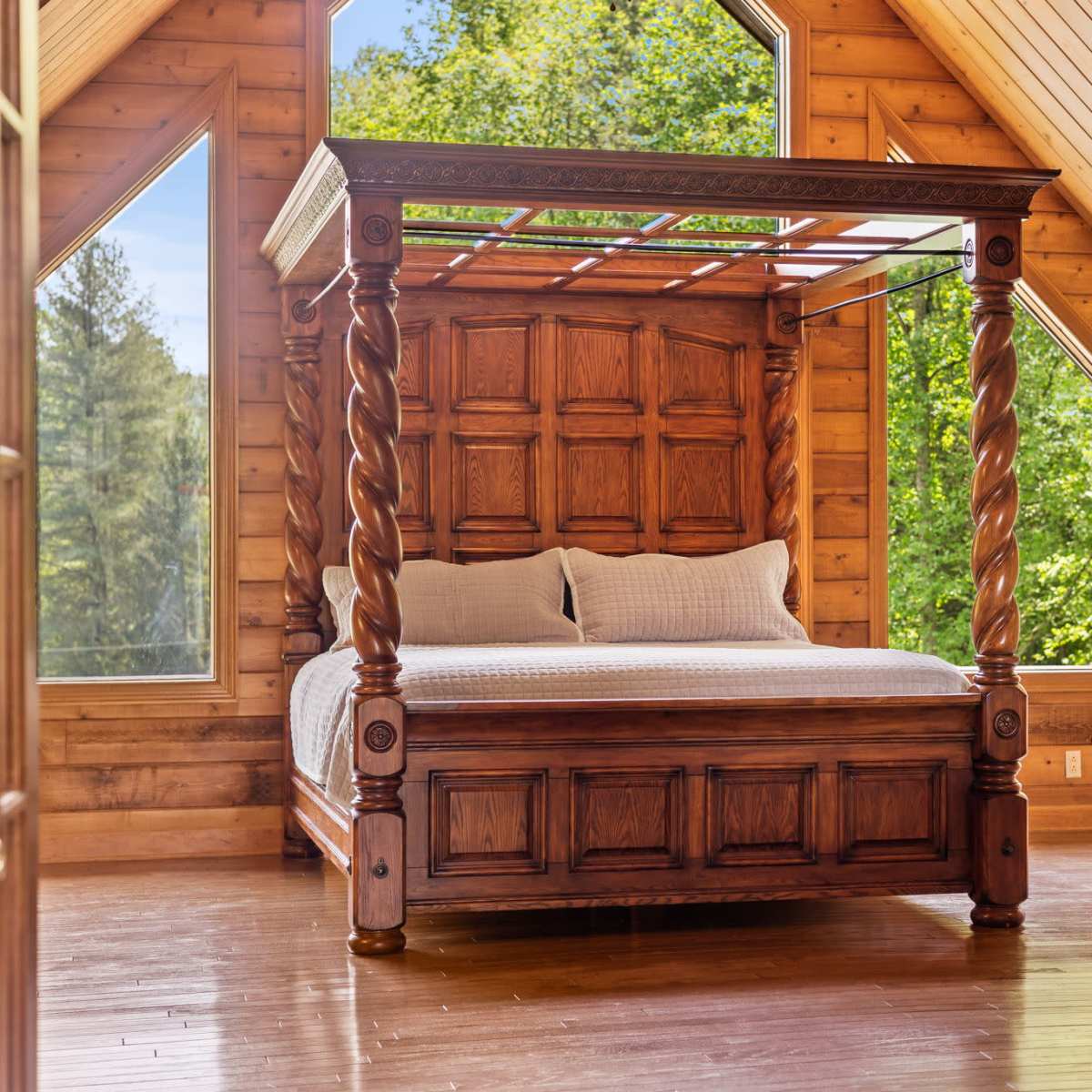 A wooden four-poster bed in a room with large windows and wooden walls, surrounded by greenery outside.