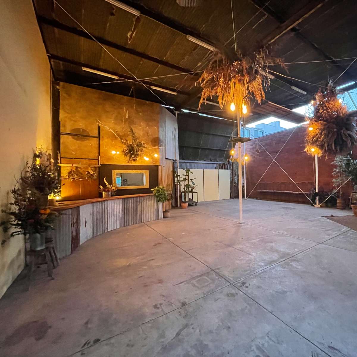 An empty industrial-style space with a wooden counter, hanging plants, and decorative lights.