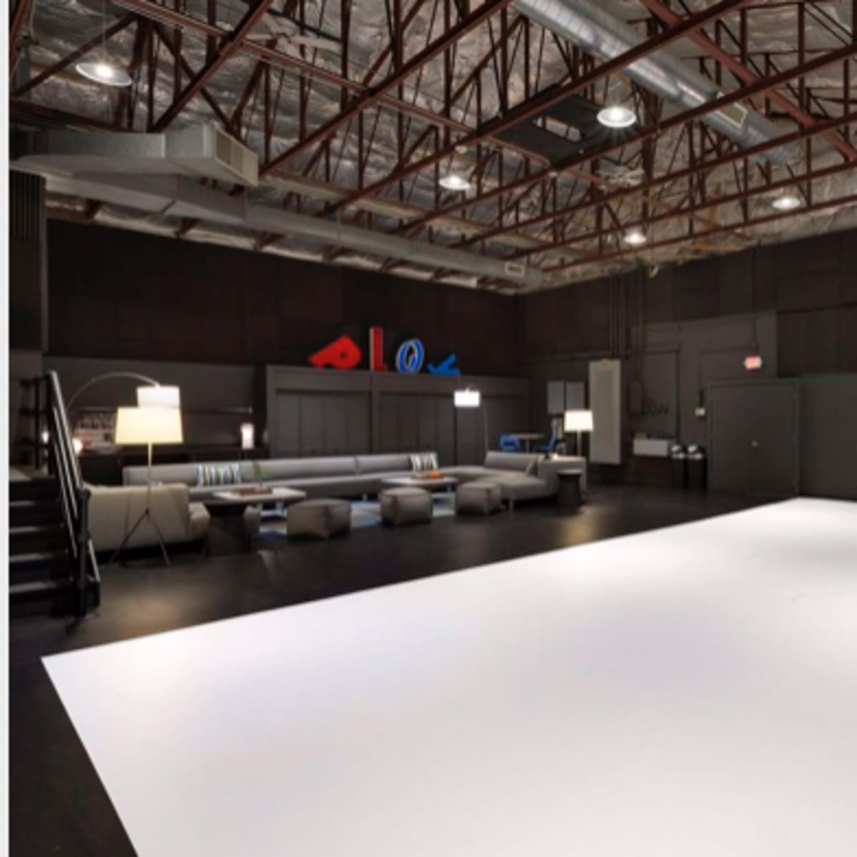 A spacious photography studio with a large white backdrop, modern seating area, and a minimalist table setup.