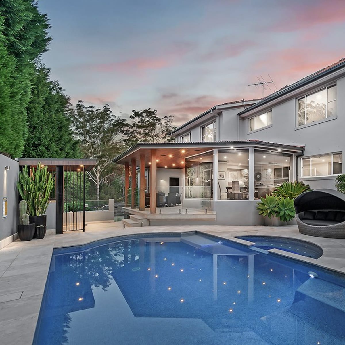 A modern backyard featuring a swimming pool, lounge chairs, and a covered patio adjacent to a two-story house.