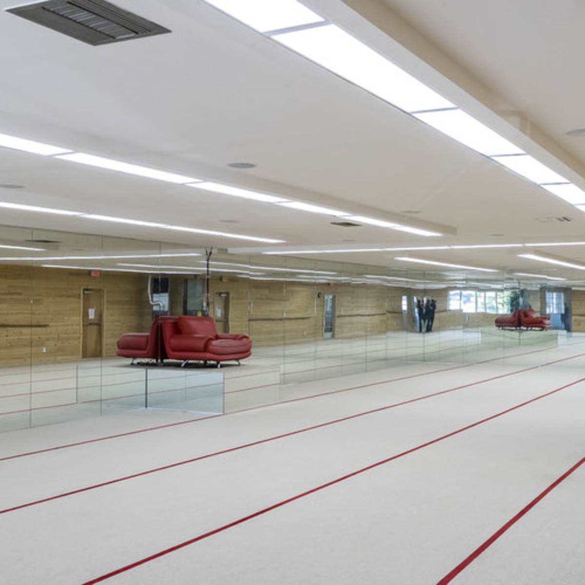 A spacious, empty indoor facility with a red and white carpeted floor and large mirrors on one wall.