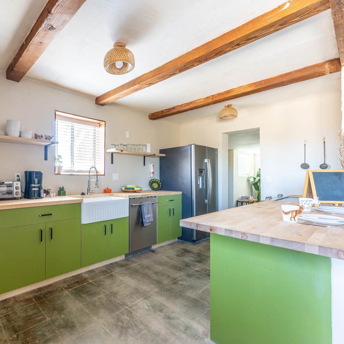 The kitchen features green cabinetry, wooden beams, and a modern layout with appliances and open shelving.