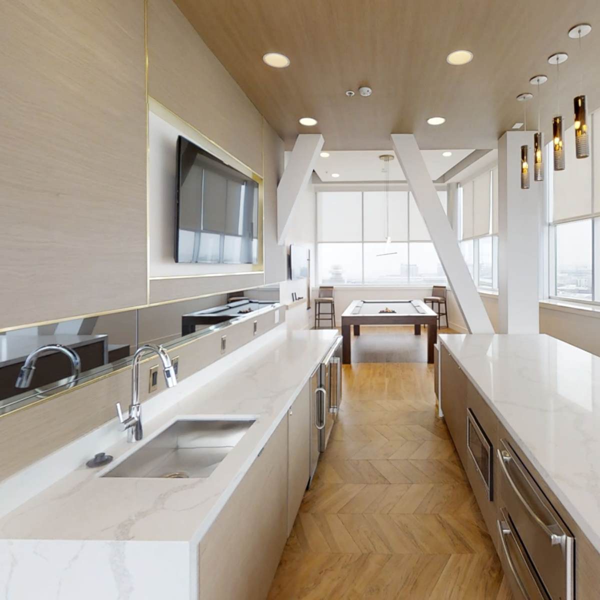 A modern kitchen with a long island counter, sleek cabinetry, and large windows offering city views.