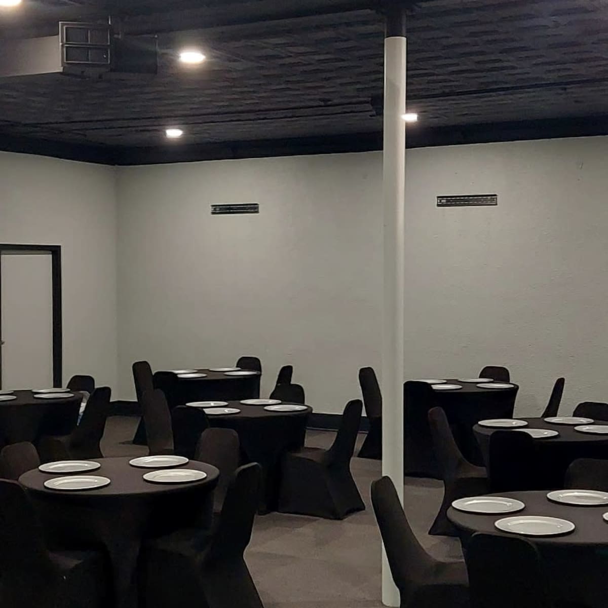 A dining area with several round tables covered by black tablecloths and white plates set on top.