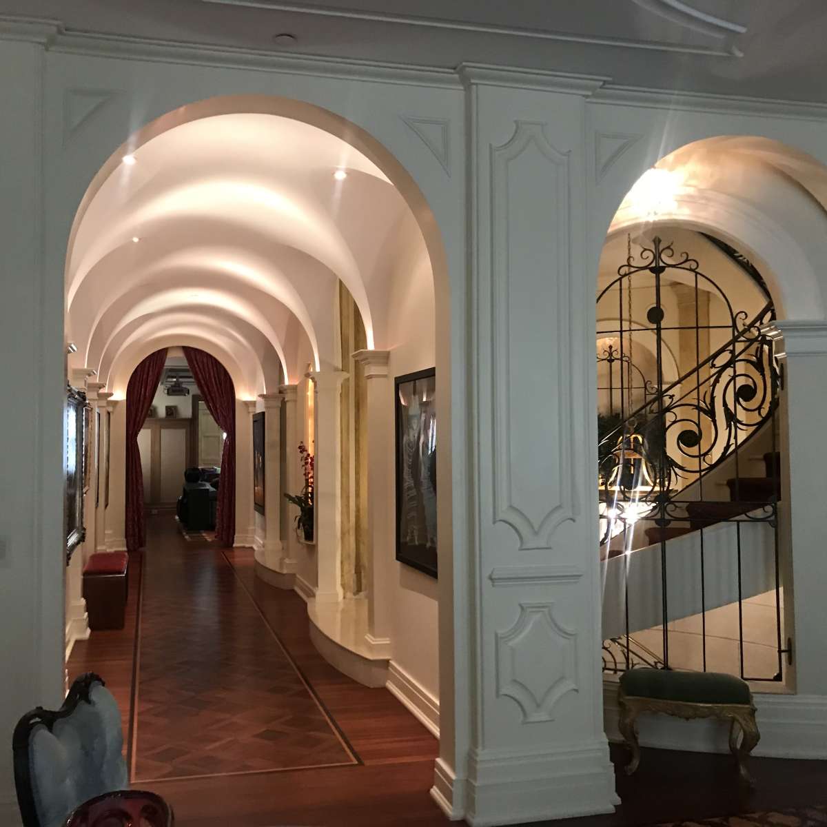 A spacious hallway with arched ceilings, framed by decorative walls, leading to a staircase and a set of curtains.