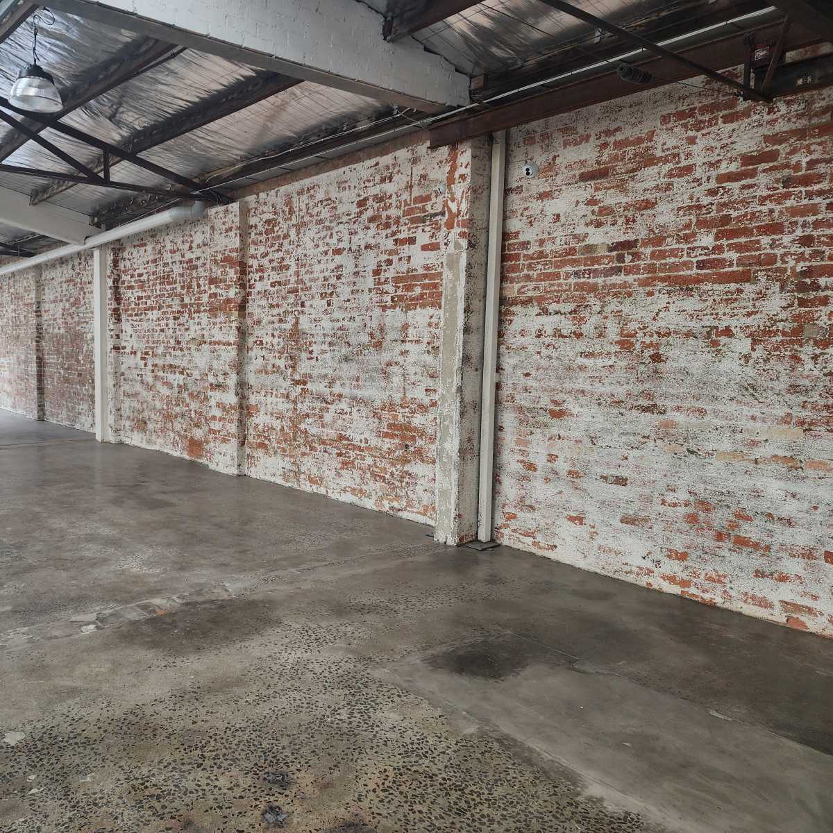 A spacious industrial room with bare brick walls and a concrete floor, illuminated by natural light from large windows.