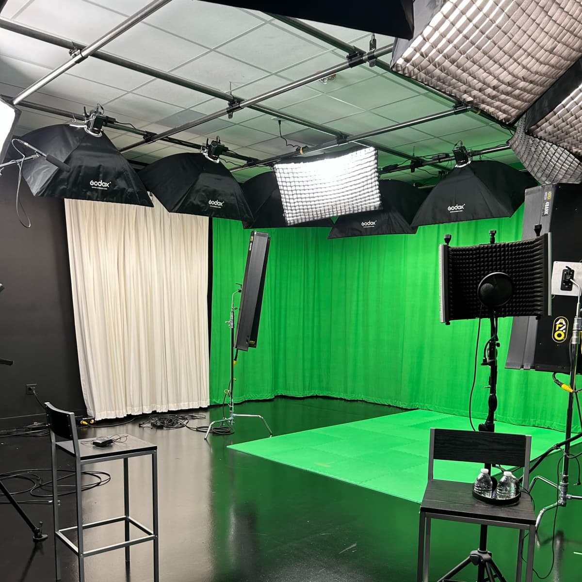 A photography studio equipped with a green screen backdrop, lighting setups, and a few chairs.