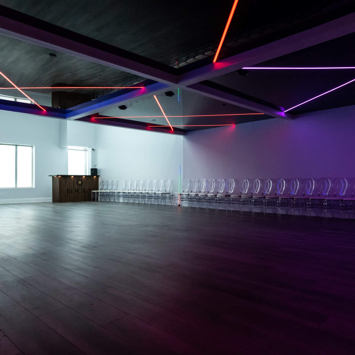 A spacious room with clear chairs arranged in a row and colorful LED lights illuminating the ceiling.