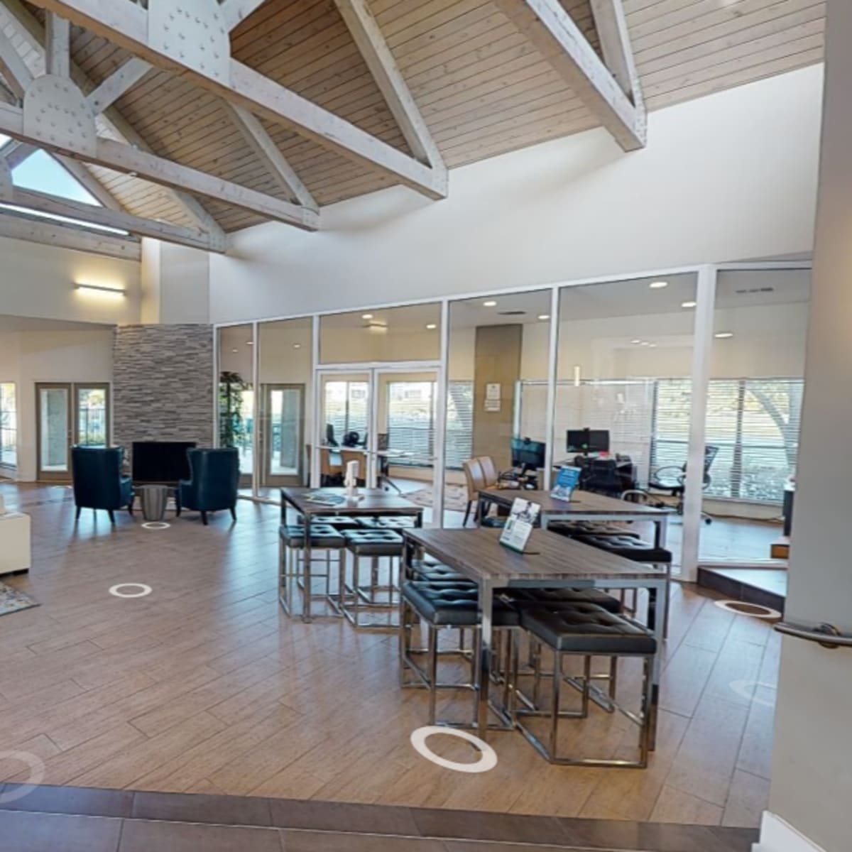 A modern community lounge with high ceilings, a seating area featuring circular ottomans, and a dining space with tables and chairs.