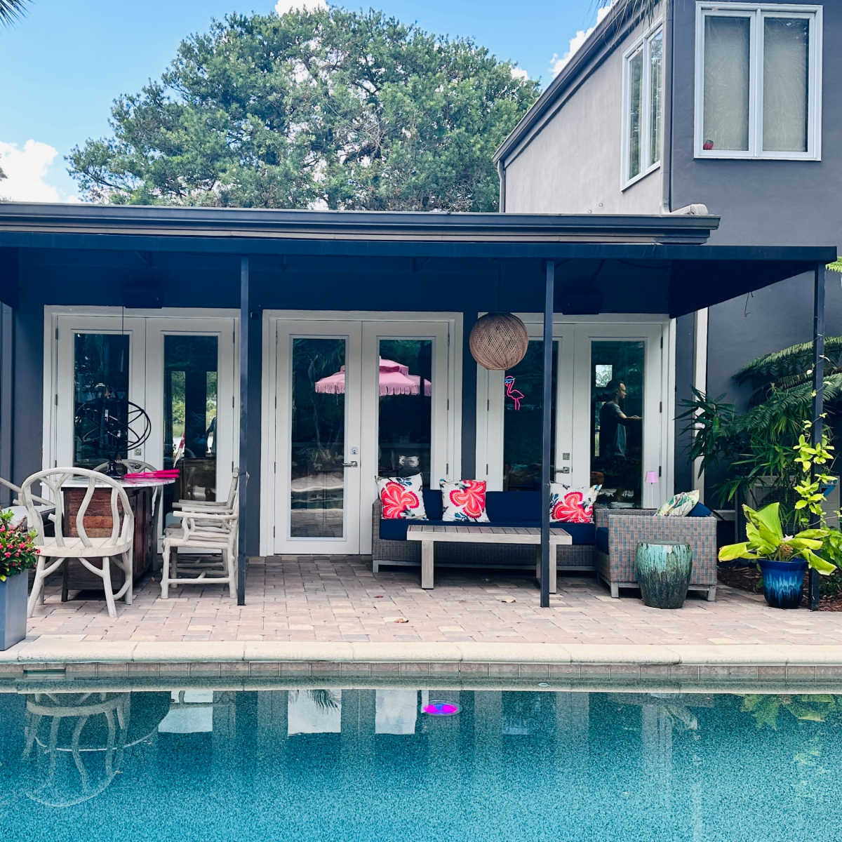 A modern patio with a pool in front features a seating area adorned with colorful flowers and tropical plants.