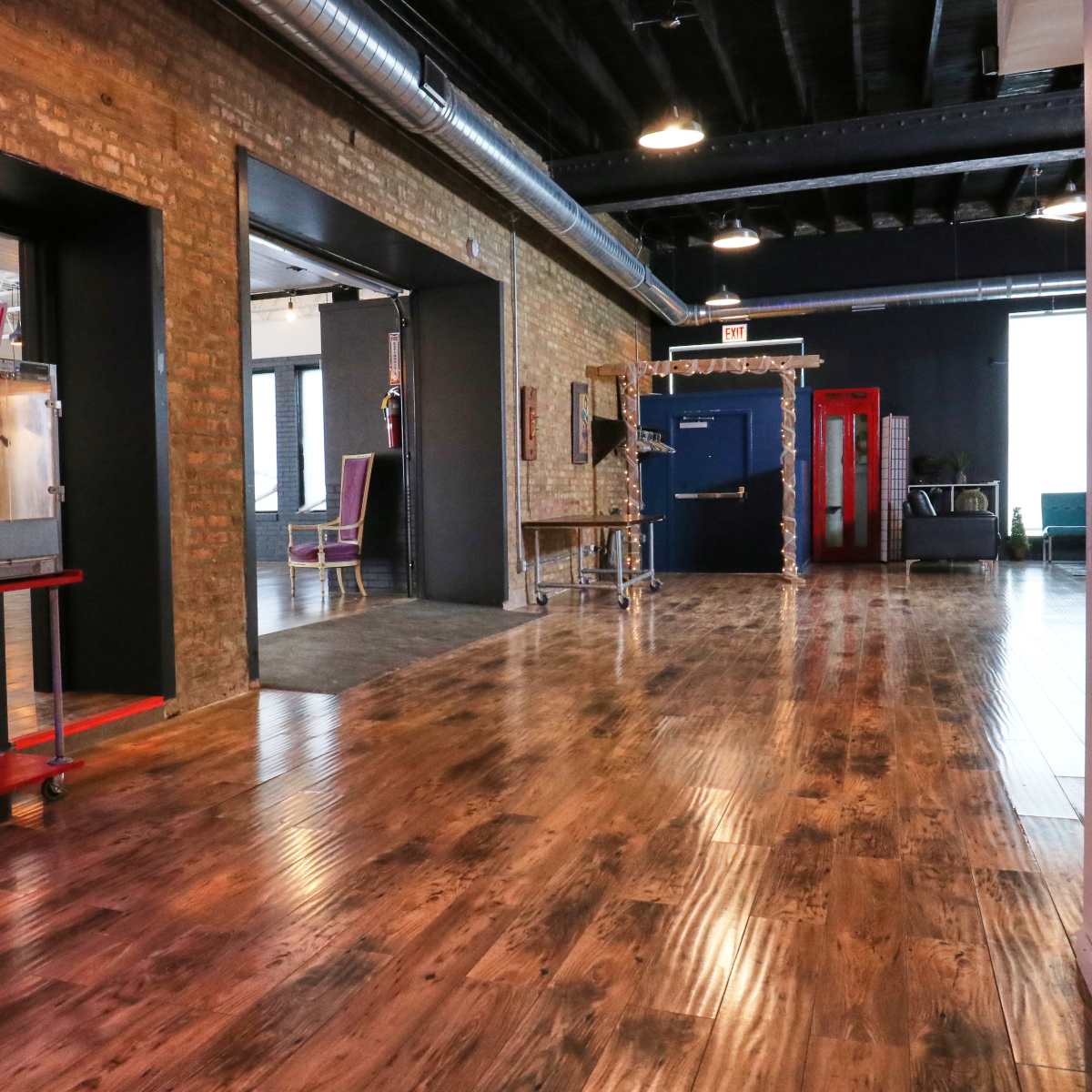 A spacious room with a polished wooden floor, exposed brick walls, and a popcorn machine on a red cart.