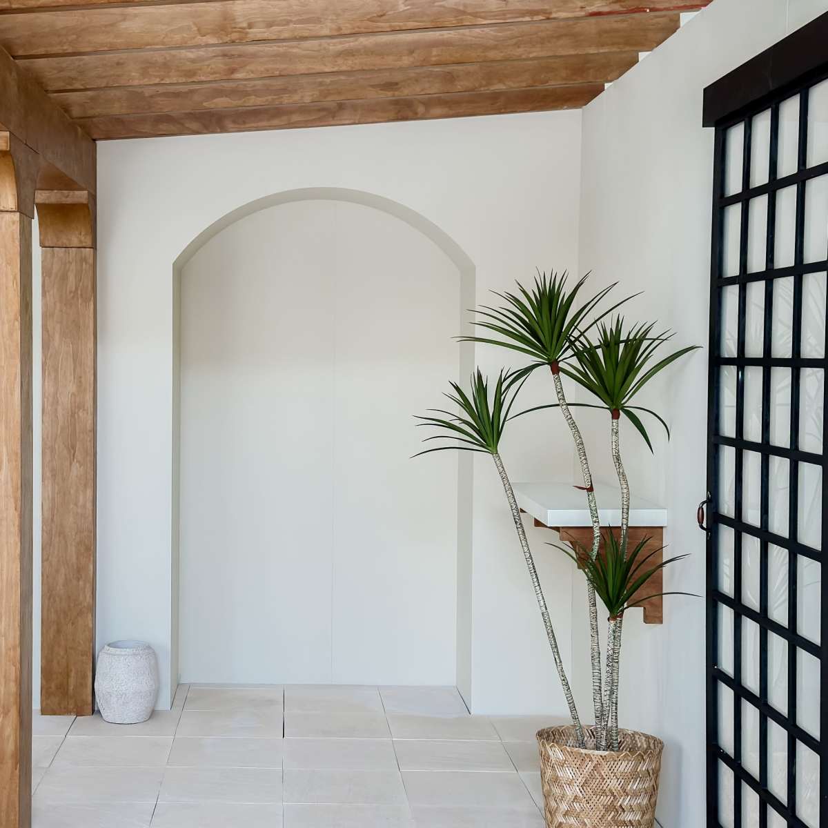 A porch area with wooden beams, a potted plant, and a decorative wall niche.