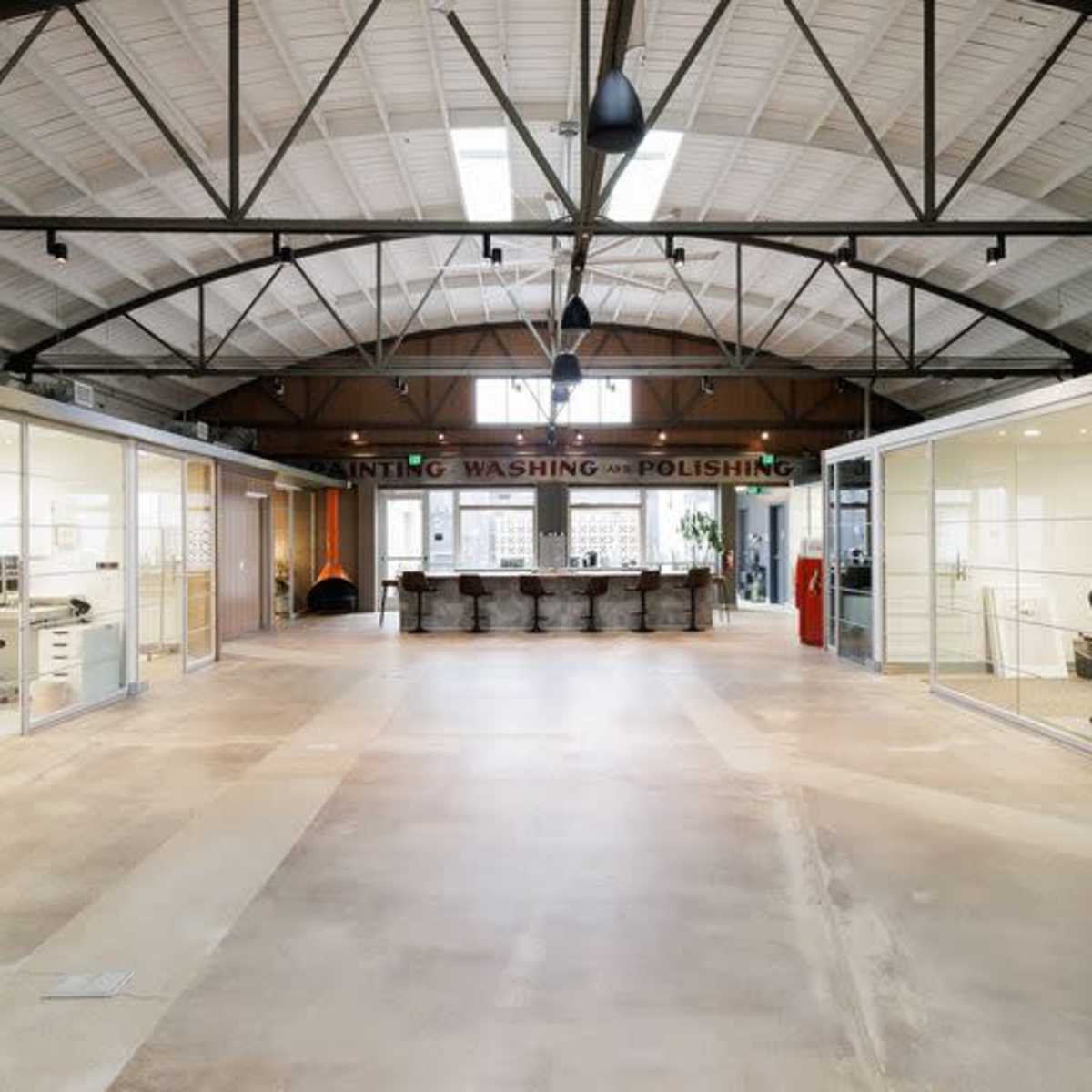 A spacious office interior with large glass walls, high ceilings, and a central area featuring a reception or collaboration space.