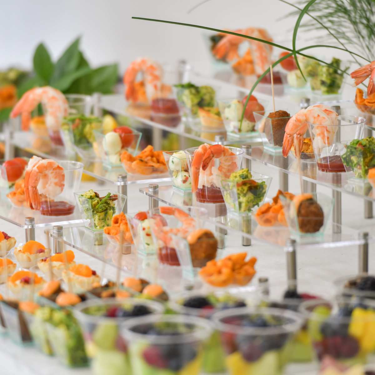 A buffet display features various appetizers and desserts arranged in clear cups on tiered stands.