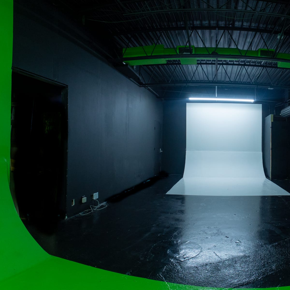 An empty photography studio featuring a green backdrop, a curved white backdrop at the center, and industrial lighting above.