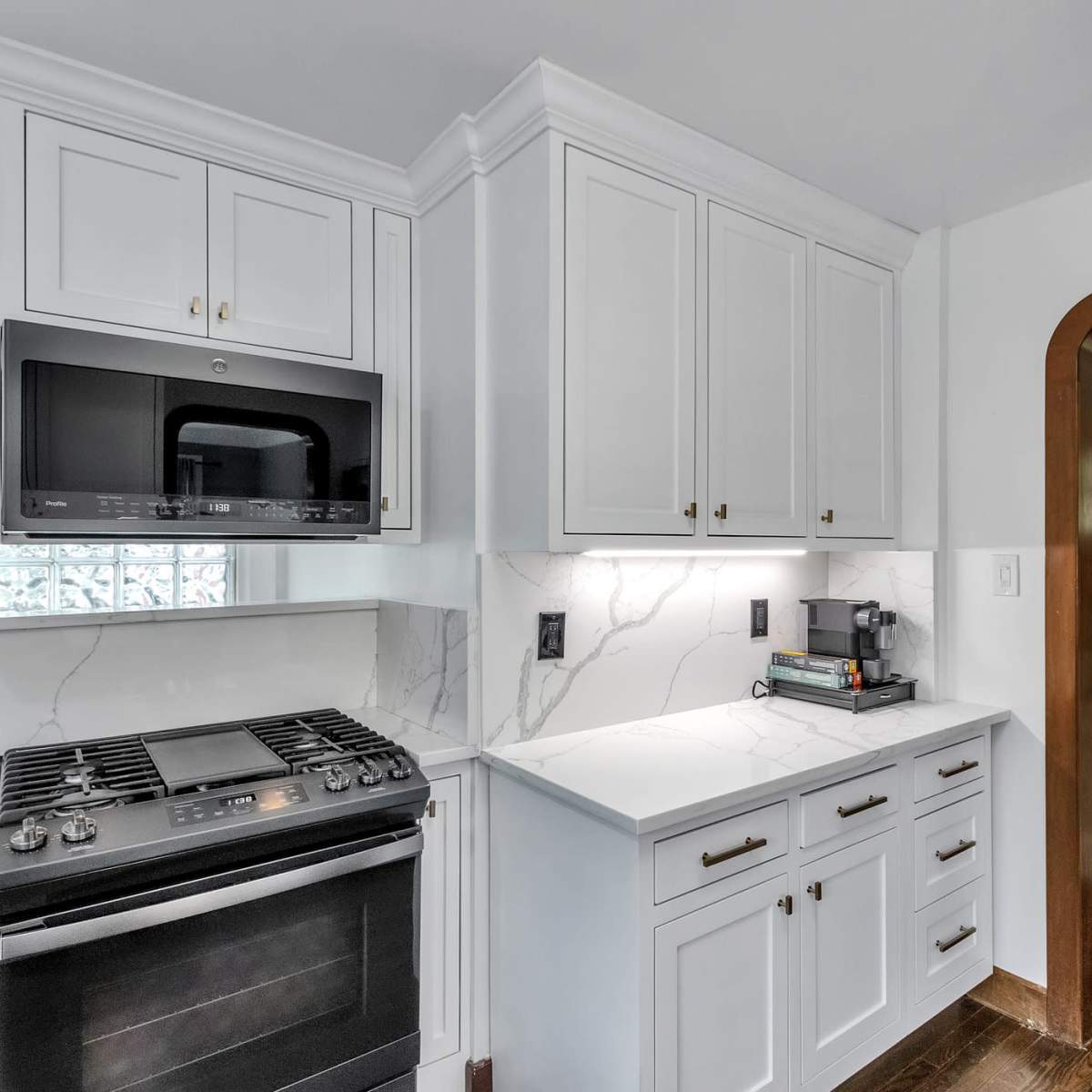 A modern kitchen with white cabinetry, a built-in microwave, and a gas stove, adjacent to an entryway leading to a staircase.