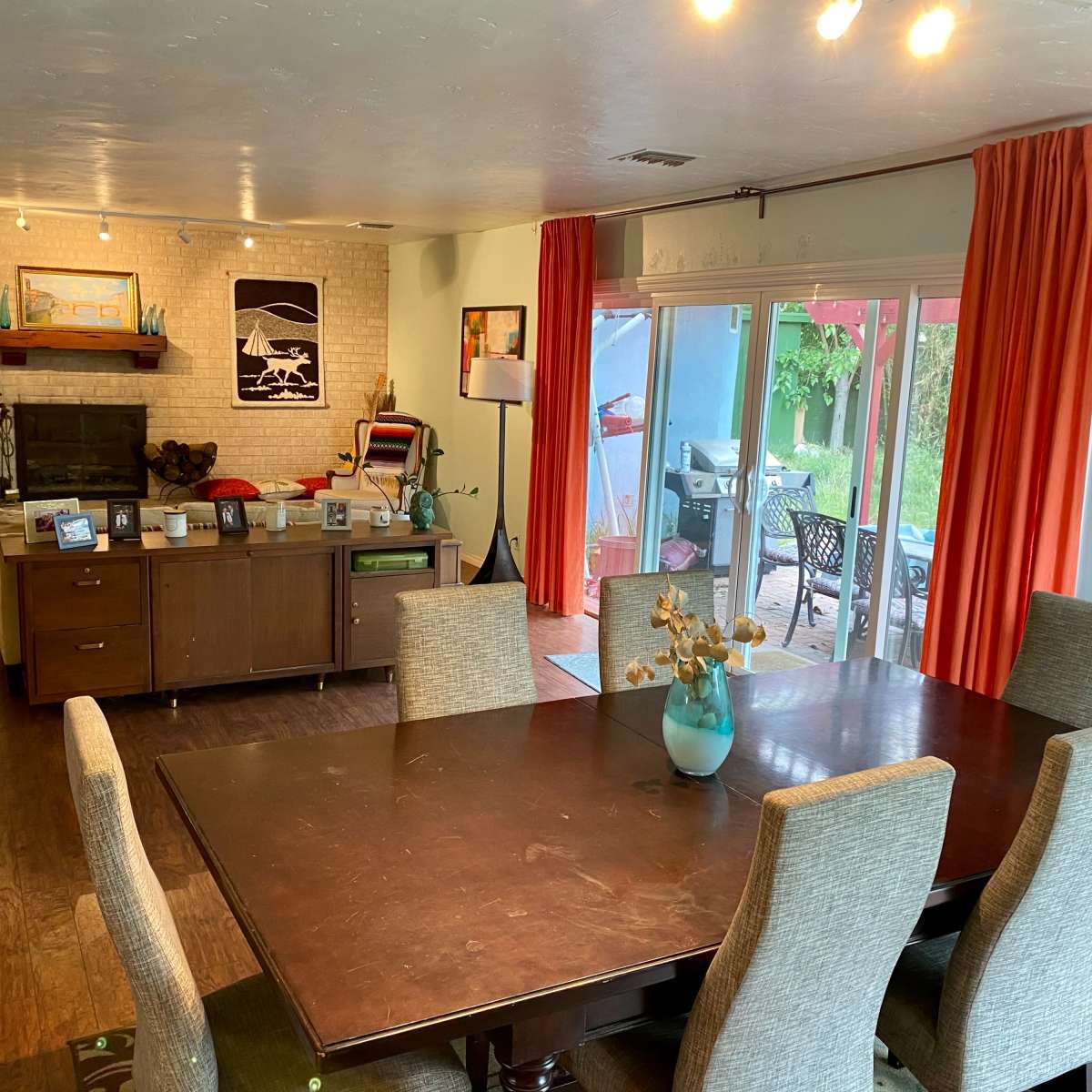 A spacious living and dining area features a wooden table with upholstered chairs, a modern kitchen island, and large windows leading to a patio.