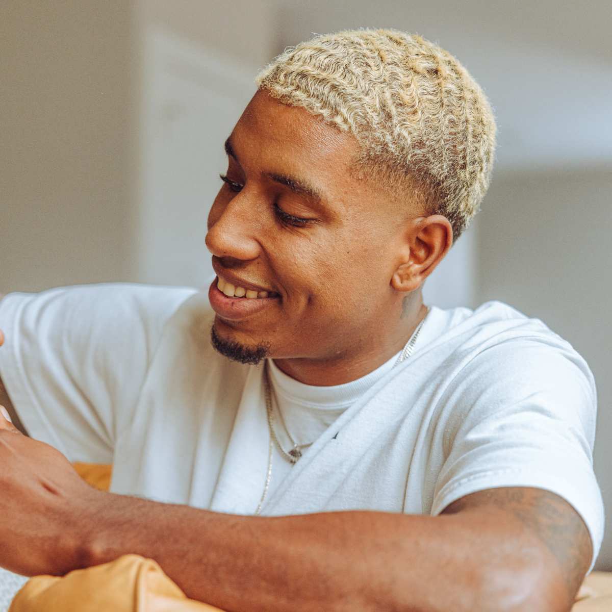 A man is sitting on a couch, smiling as he opens a yellow bottle of a product.