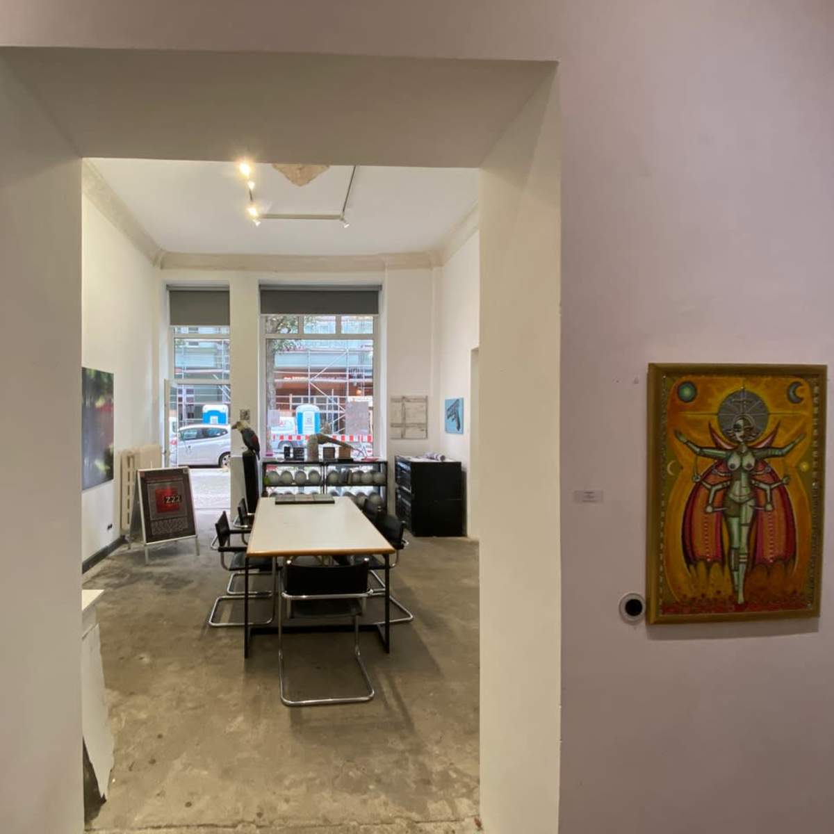 A modern, minimalistic meeting room with a large table surrounded by chairs, framed by an archway and artworks displayed on the walls.