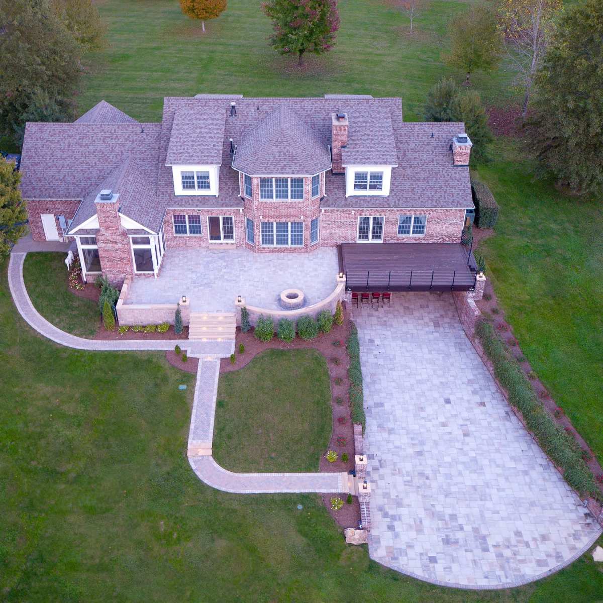 An aerial view shows a large brick house with a landscaped yard, stone pathway, and a patio area in front.