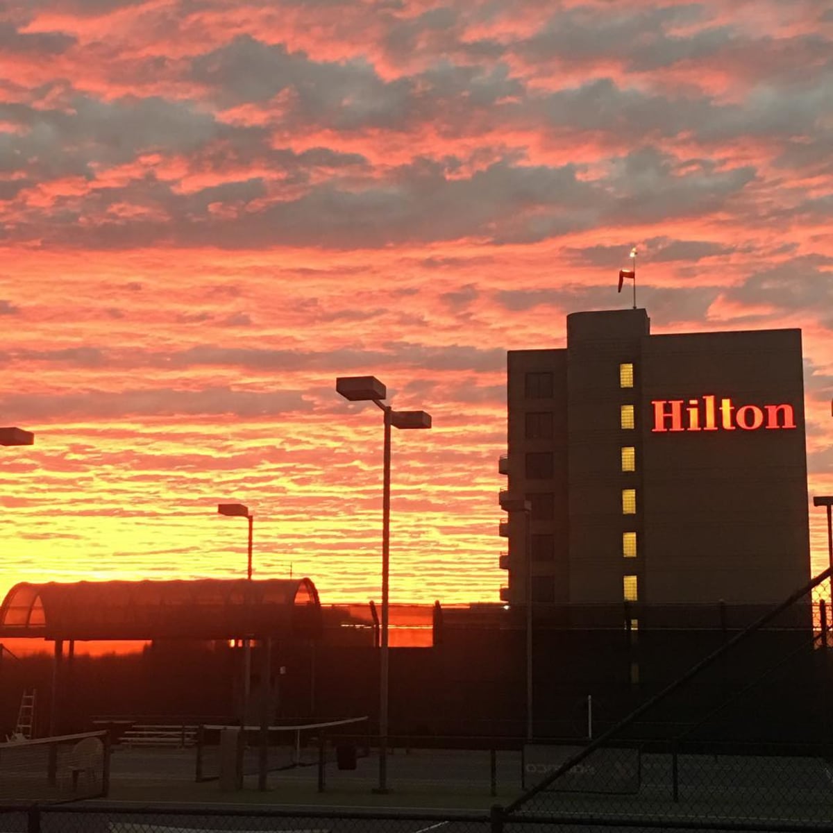 The Hilton hotel stands against a vibrant sunset sky filled with clouds.