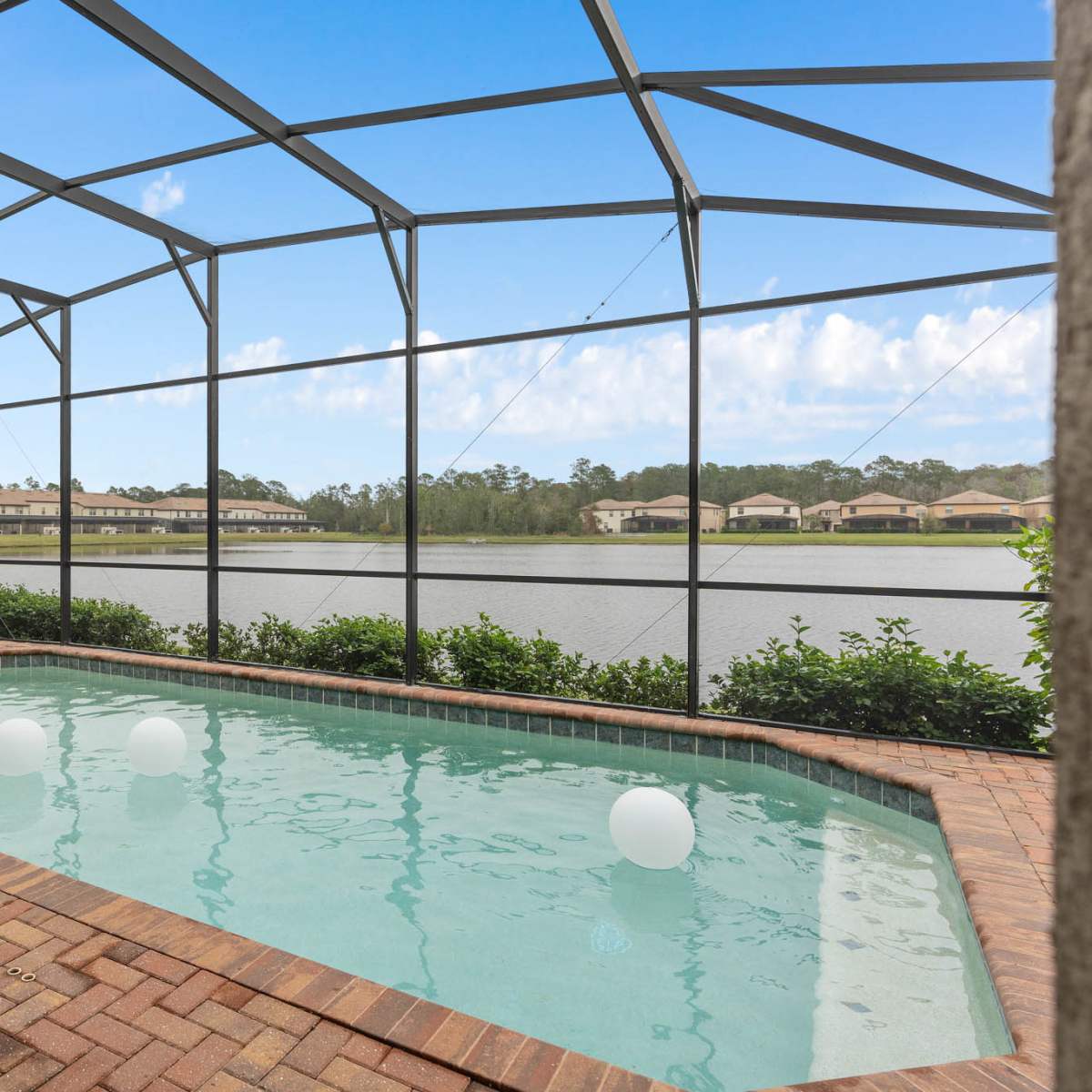 A screened-in pool area with a small spa, surrounded by brick paving and overlooking a calm lake.