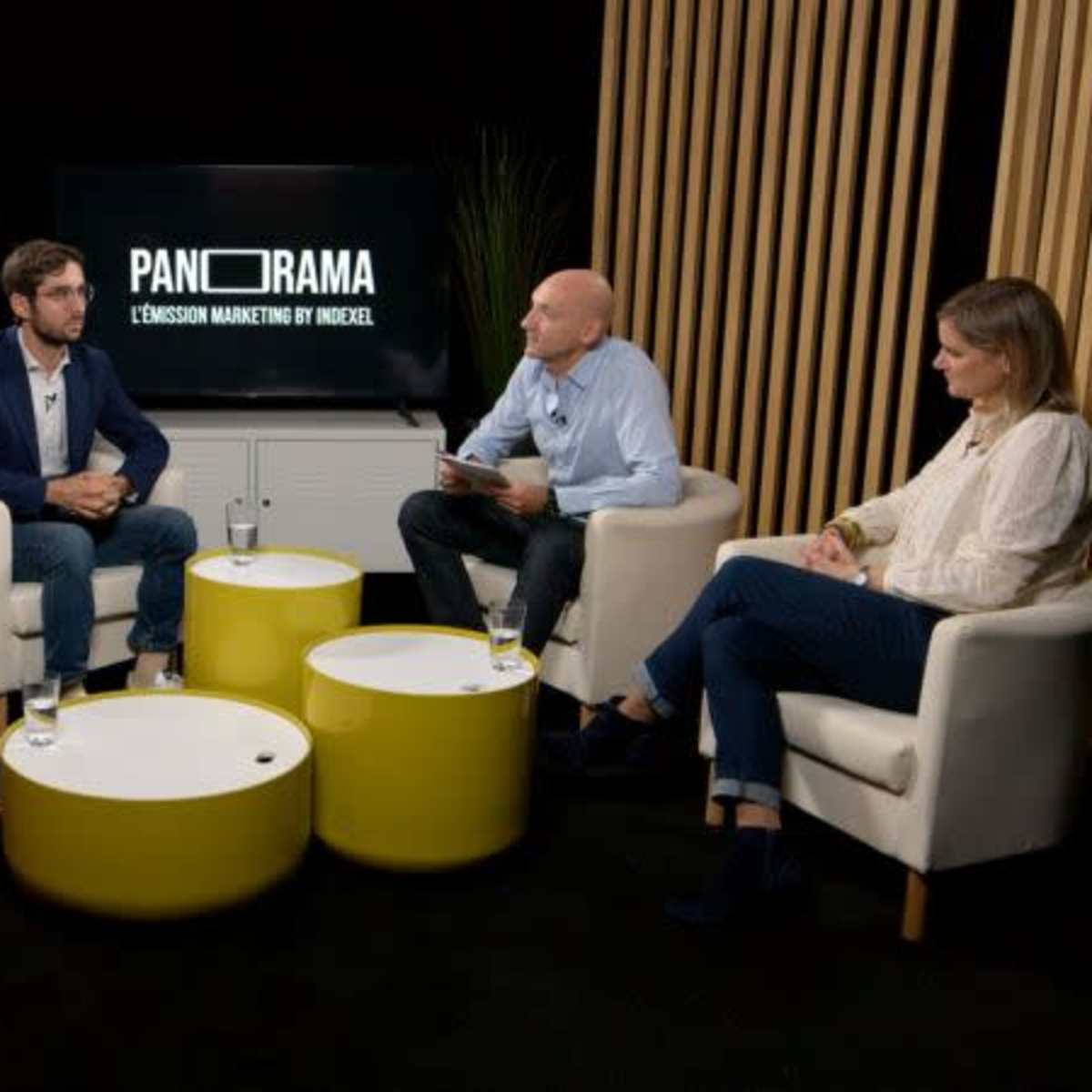 A group of four people seated around small tables in a modern studio setting, participating in a discussion on marketing.