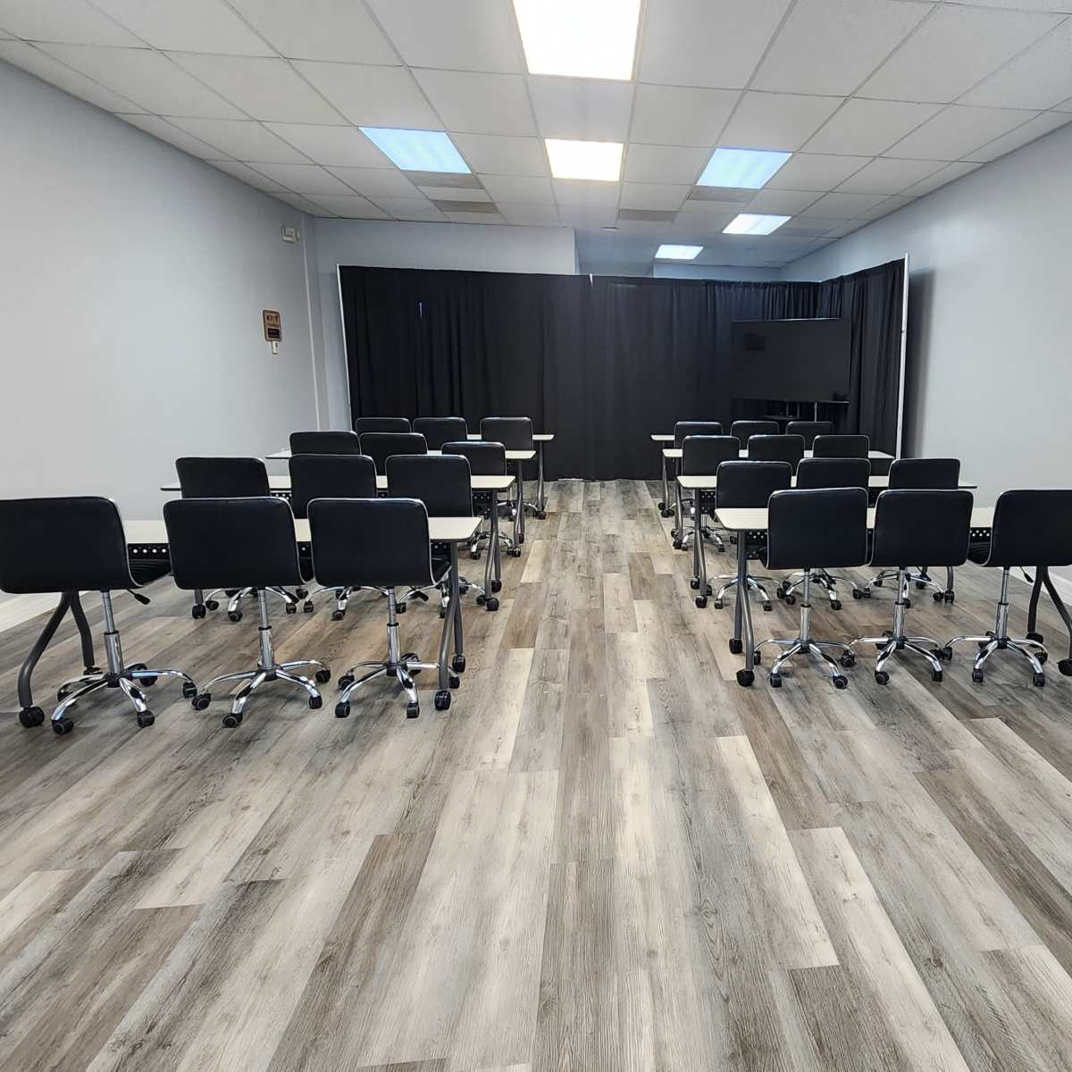 A modern meeting room features rows of black chairs on wheels facing a front area with a table and decorative flowers.