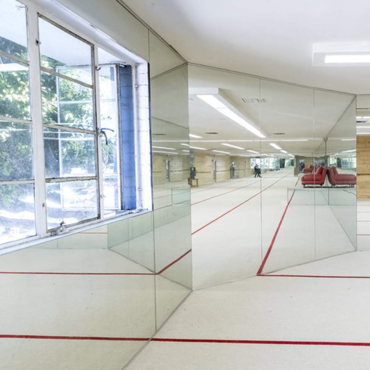 A room with mirrored walls and red lines on the floor, featuring large windows that allow natural light to enter.