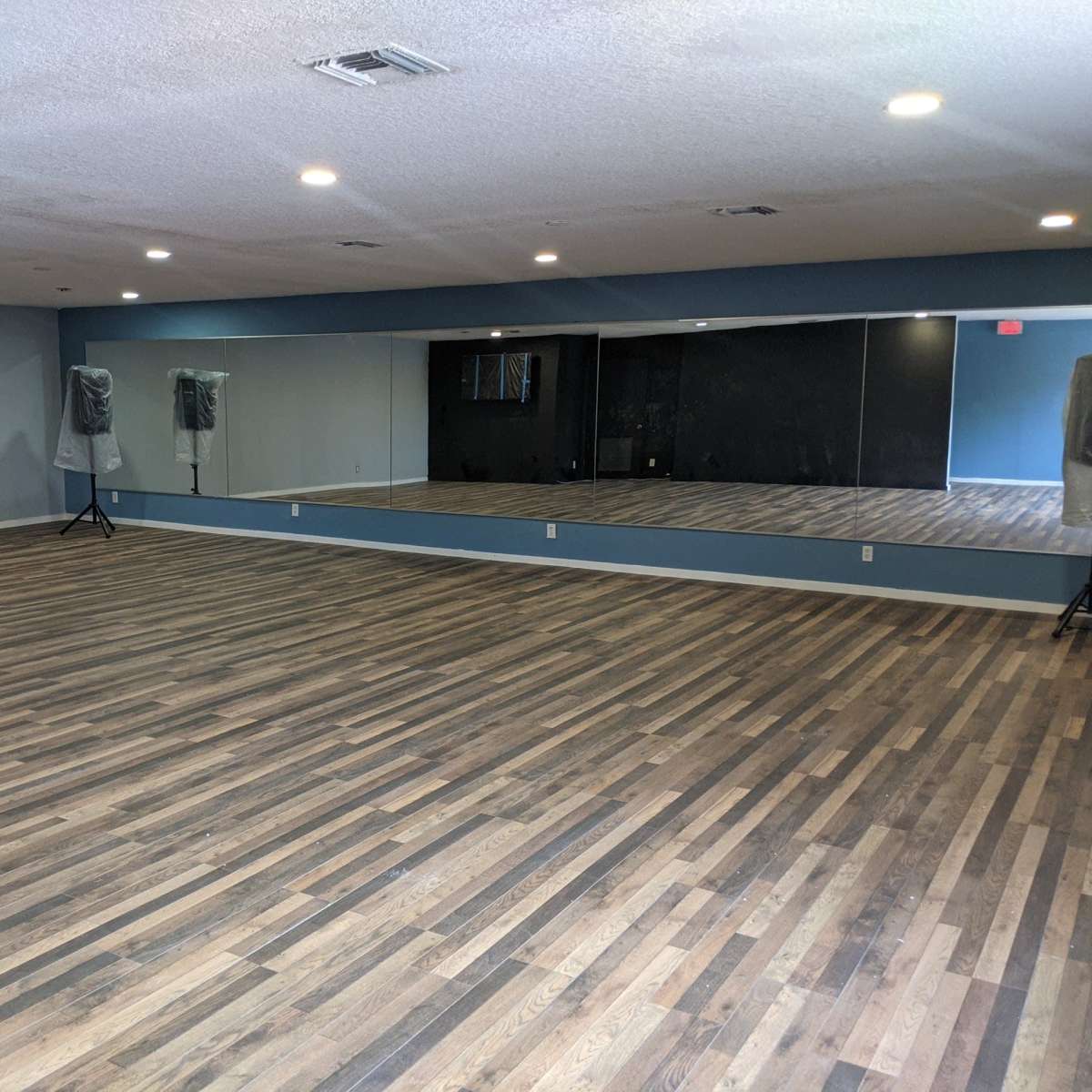 An empty dance studio with wooden flooring and large mirrors on one wall.