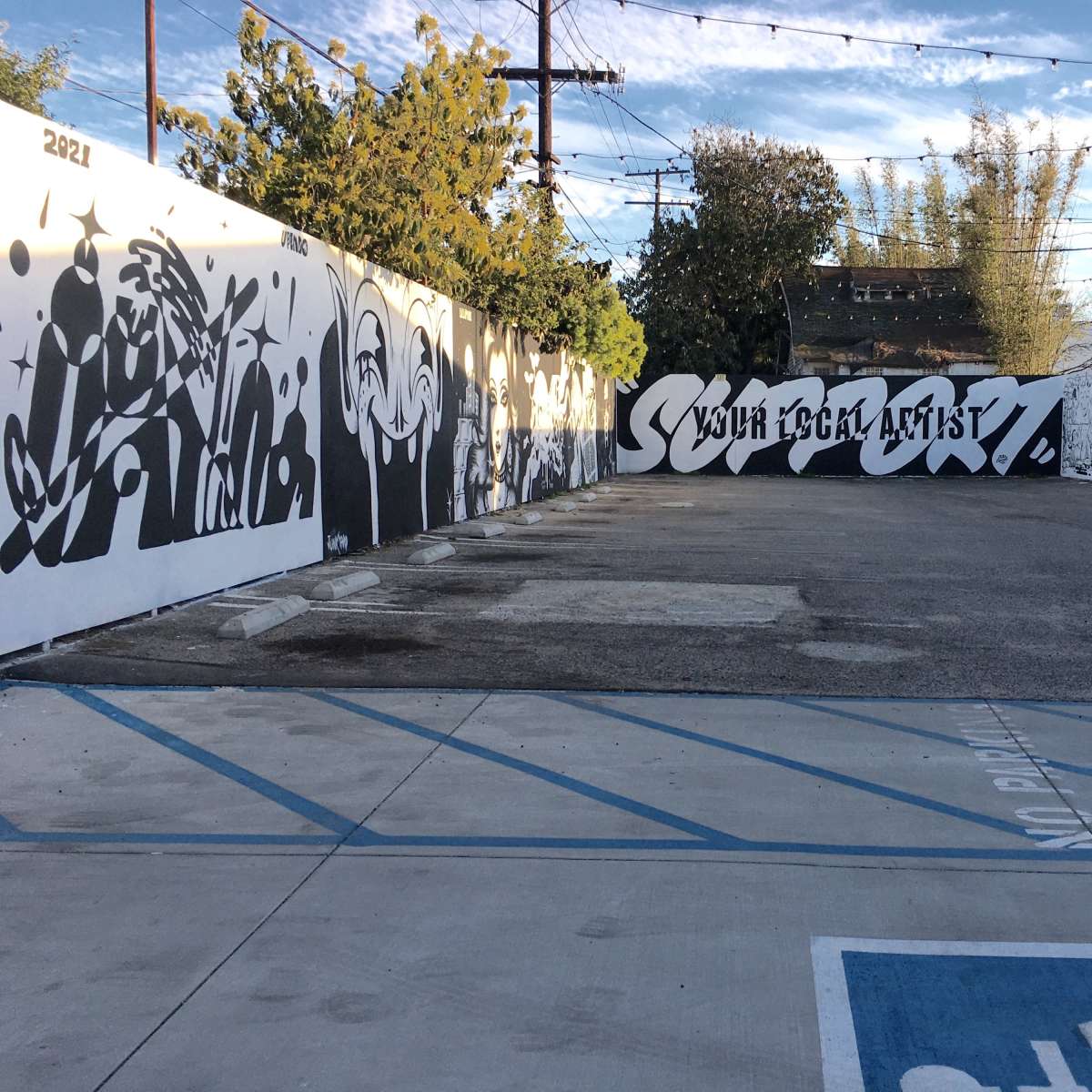 A graffiti-covered wall in an open area with a parking lot marked for accessible parking.
