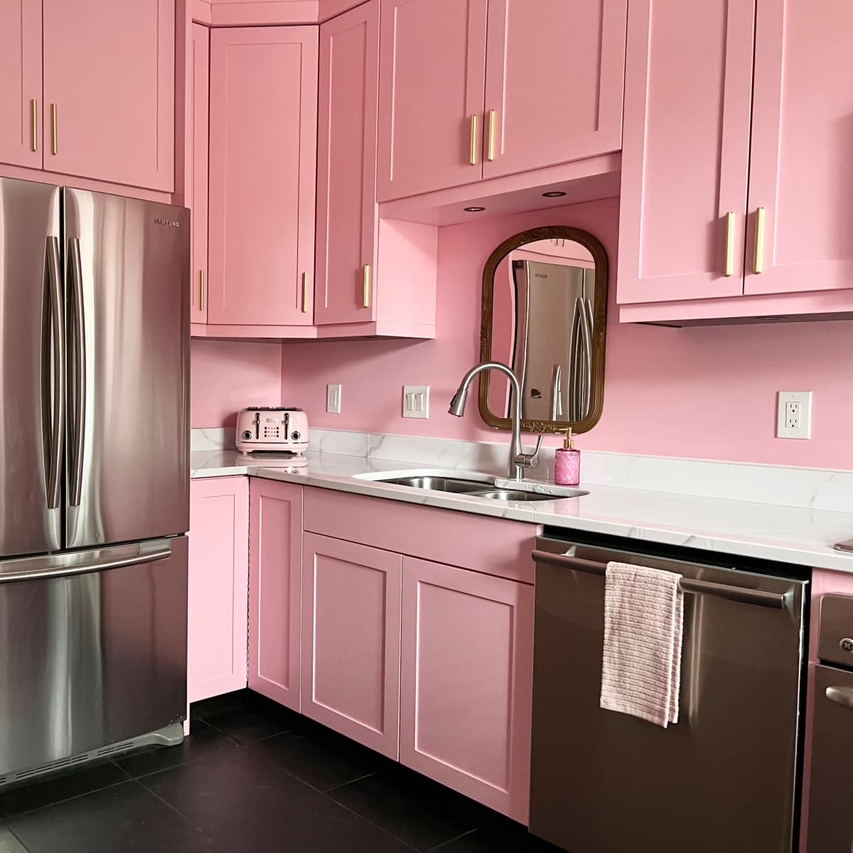 A modern kitchen features pink cabinets, a stainless steel refrigerator, and a sink with a mirror above.