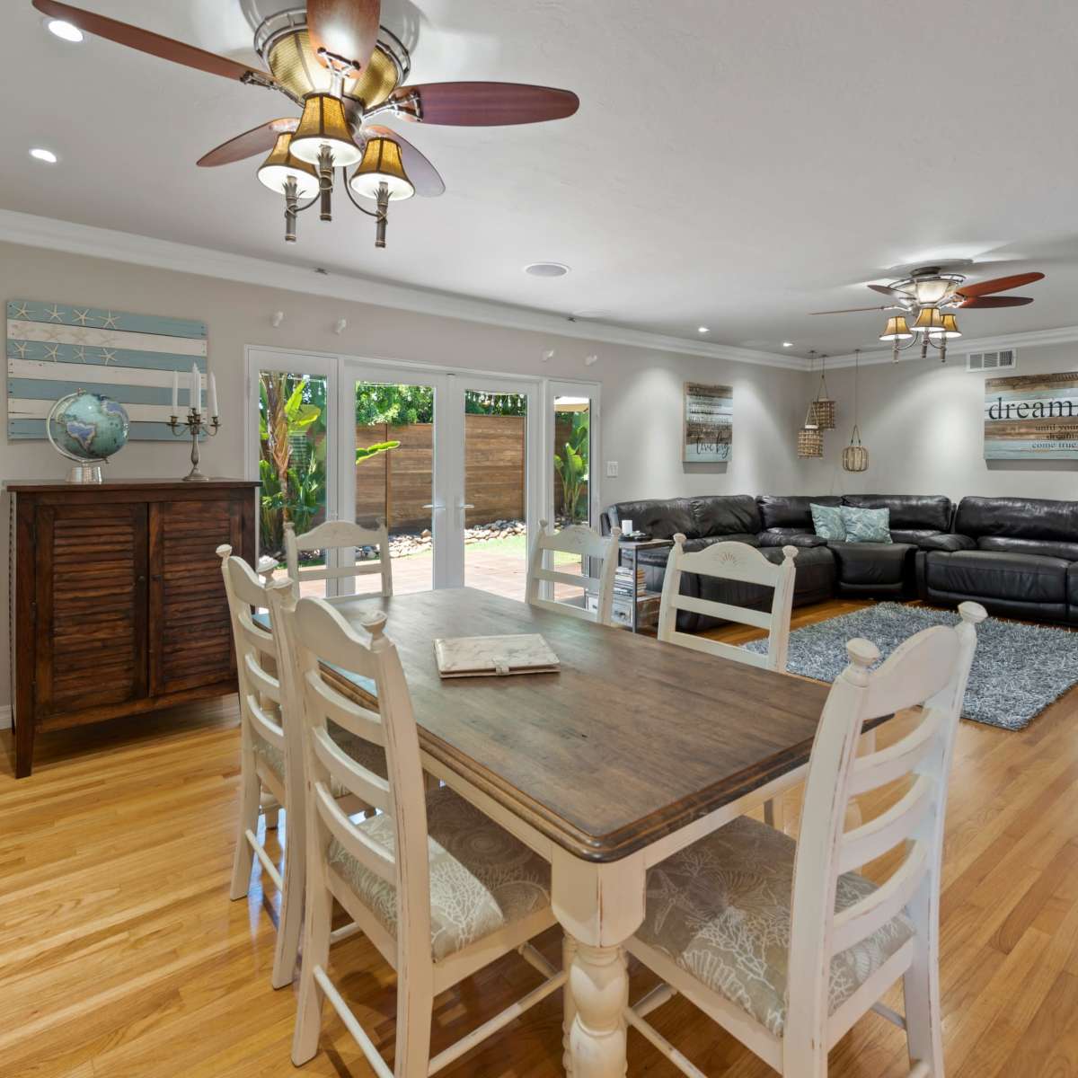 A spacious living and dining area features a wooden table surrounded by white chairs, a leather sectional sofa, and large sliding glass doors leading to an outdoor space.