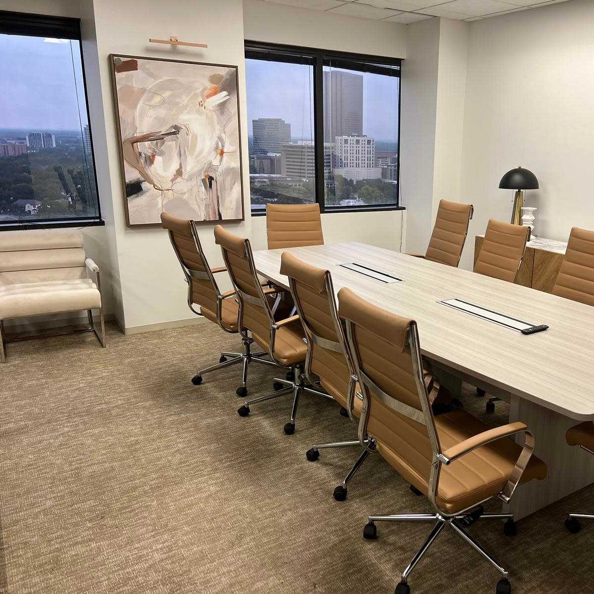 A modern conference room featuring a long wooden table surrounded by eight leather chairs, with large windows overlooking a cityscape.