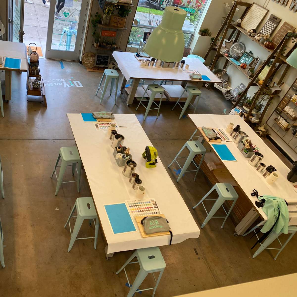 An art studio with several tables covered in white tablecloths, each set with art supplies and stools arranged around them.