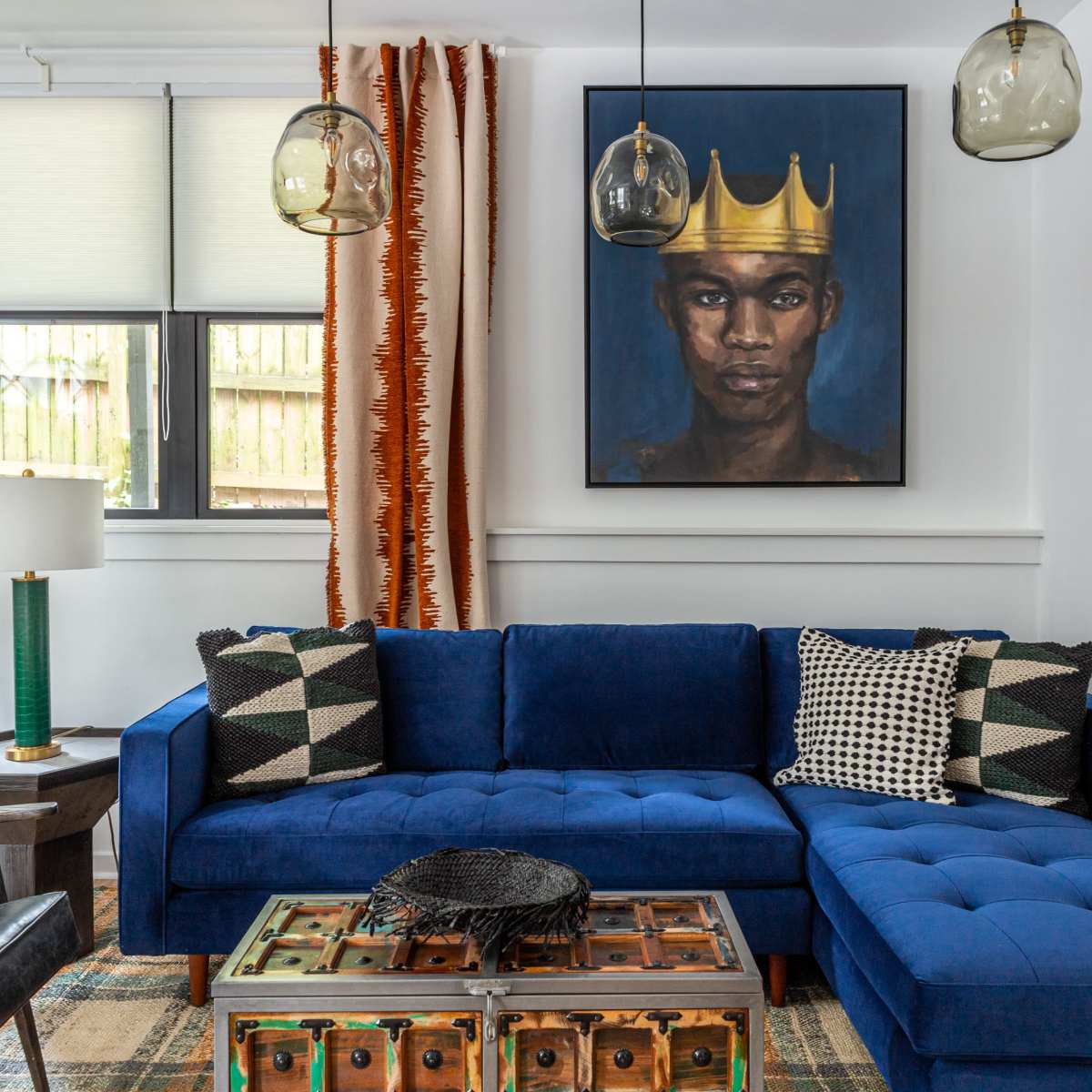 A living room with a blue sectional sofa, a wooden coffee table, decorative pillows, and a large portrait of a man wearing a crown on the wall.