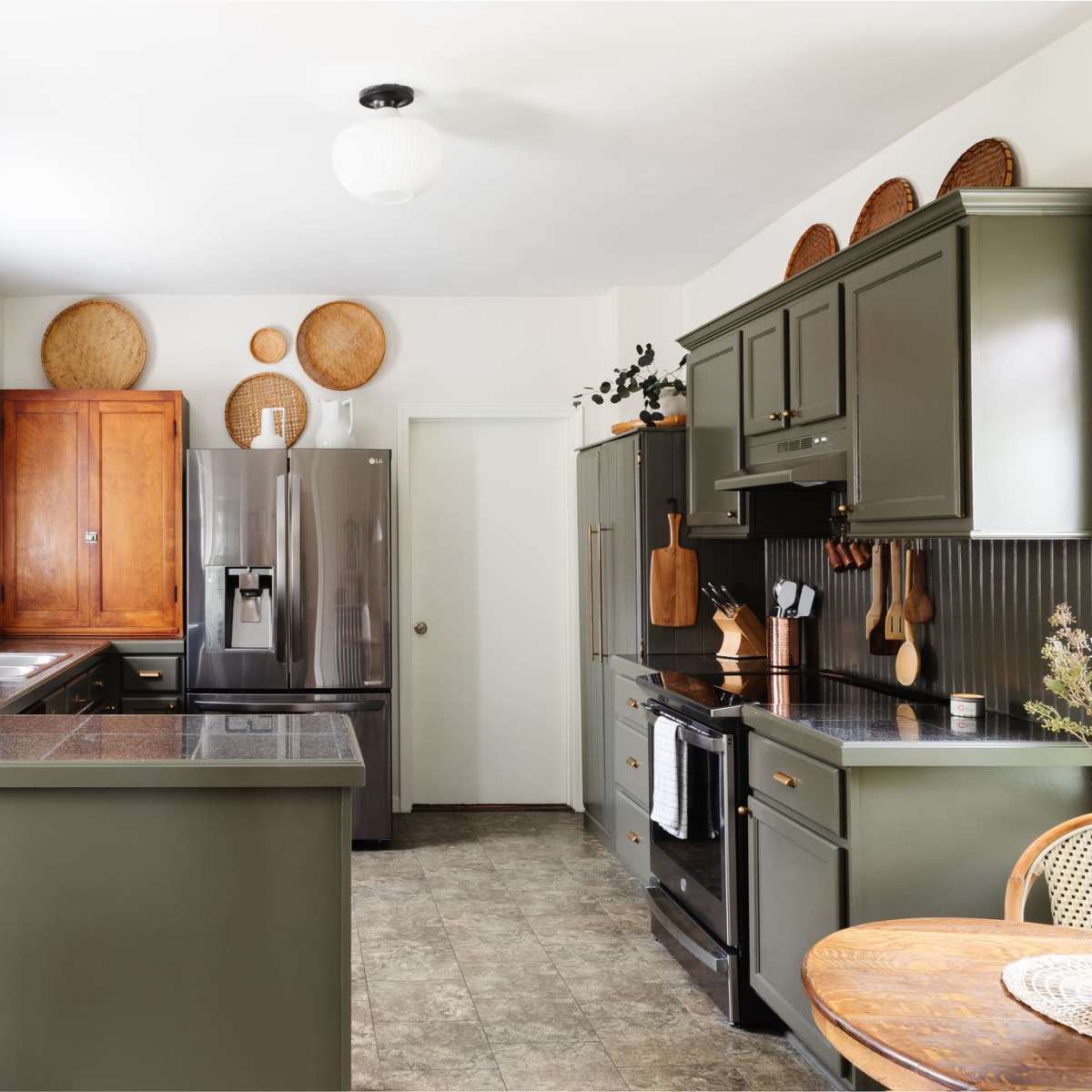 A modern kitchen featuring dark green cabinetry, stainless steel appliances, and a round dining table with woven decor elements.