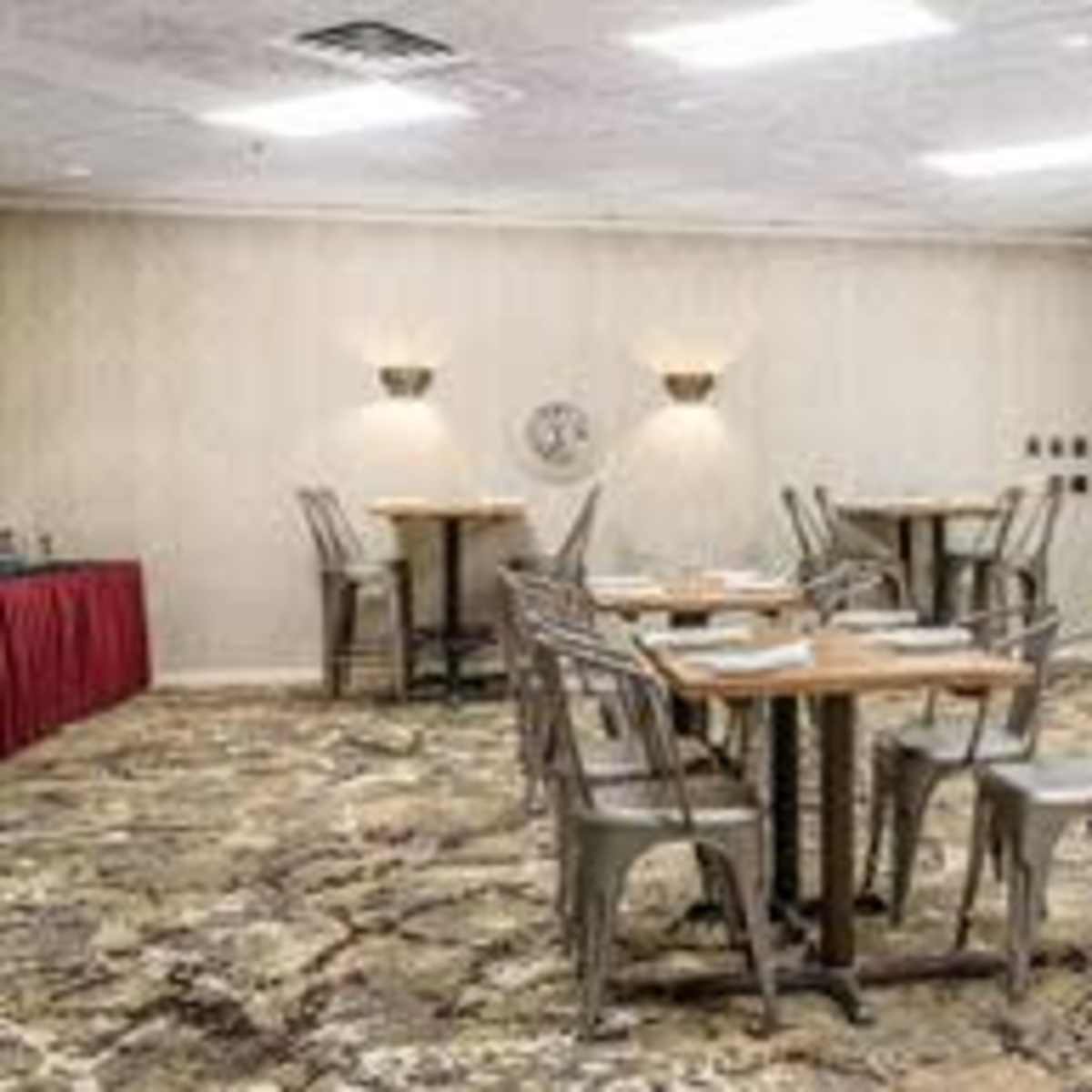 A dining area with several tables and metal chairs arranged on a patterned carpet.