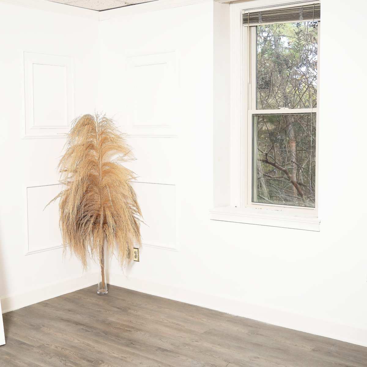 A bright, empty room with a tall mirror and a decorative dried plant near a window.