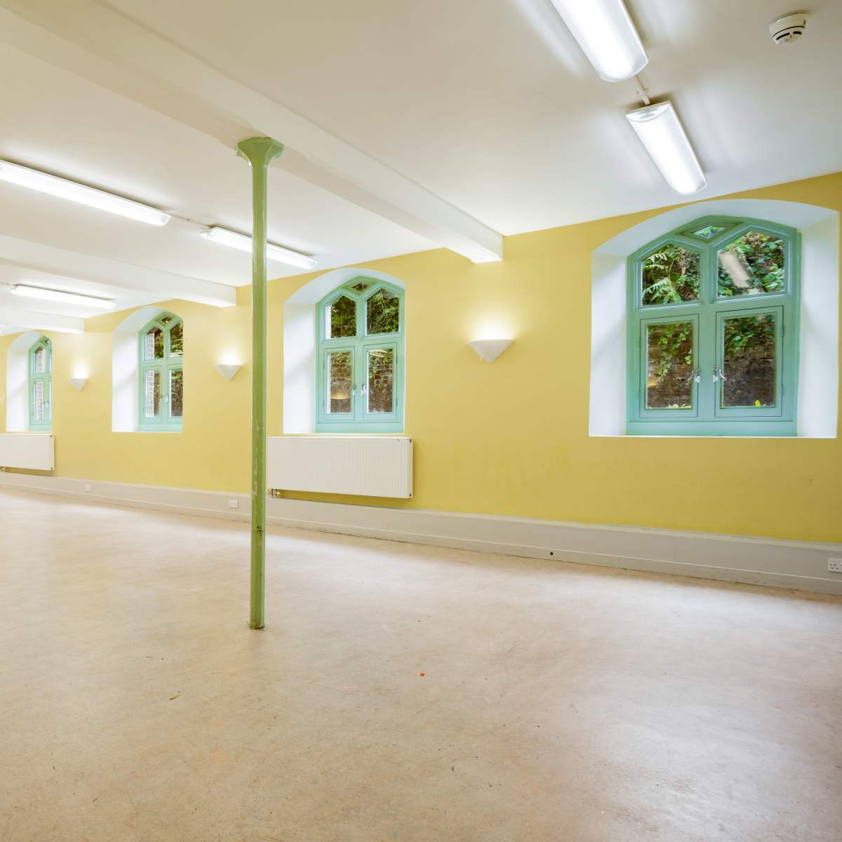 A spacious interior room with yellow walls, arched windows, and green columns.
