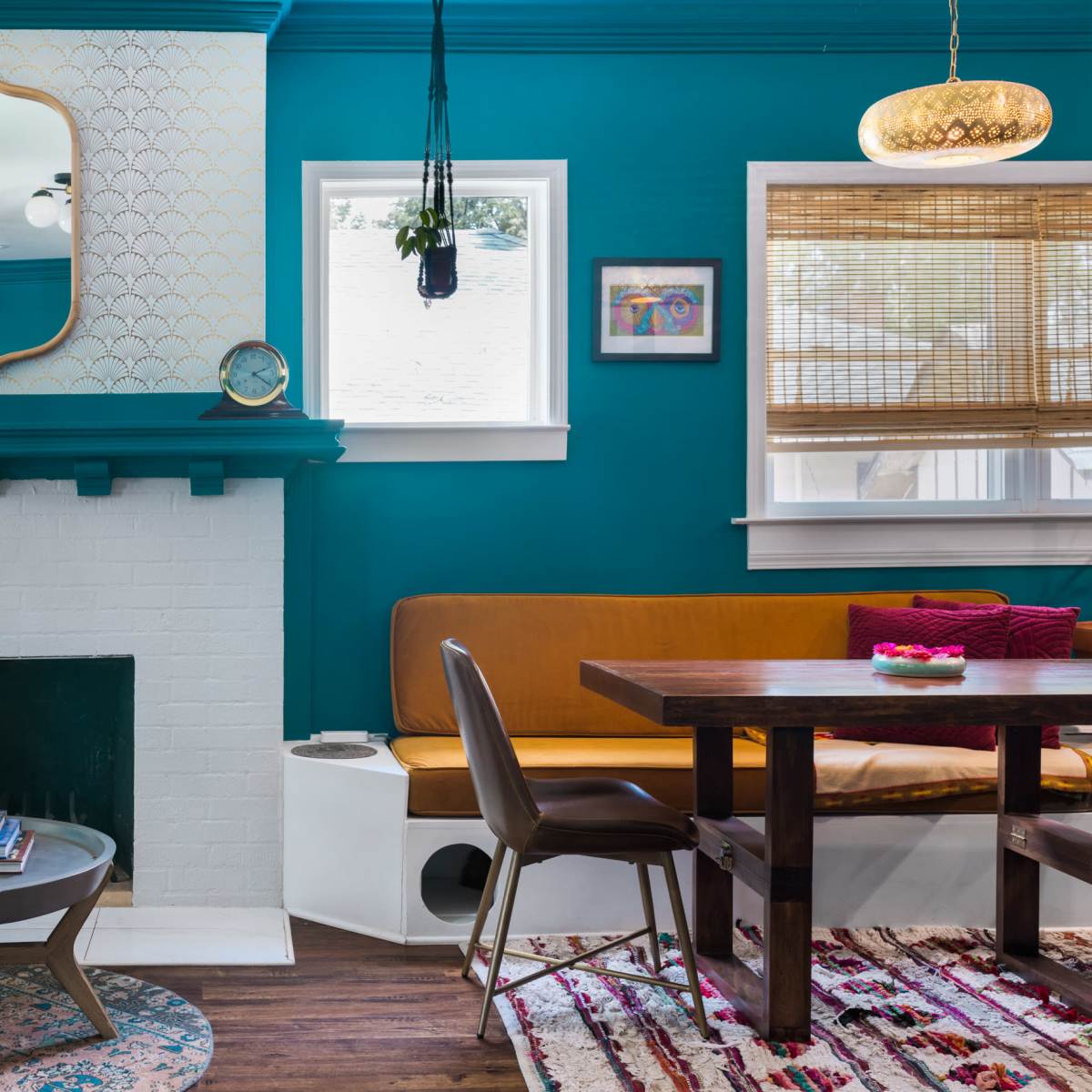 A bright teal living room featuring a fireplace, a wooden table, seating areas, and large windows with shades.